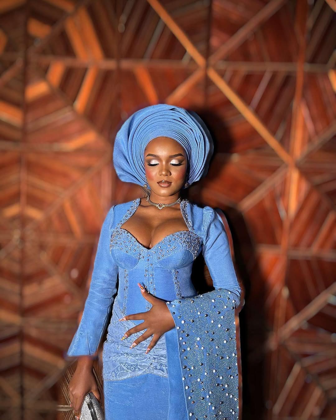 Client in a blue gele with eyes closed showing silver shimmer lids
